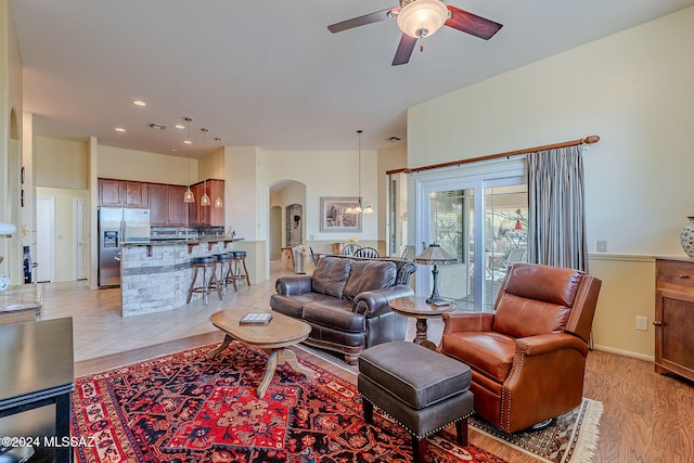 living room featuring ceiling fan with notable chandelier and light hardwood / wood-style flooring