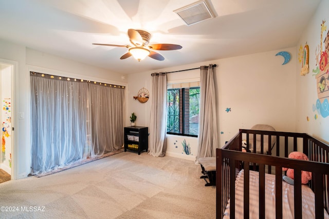 bedroom featuring ceiling fan, light colored carpet, and a crib