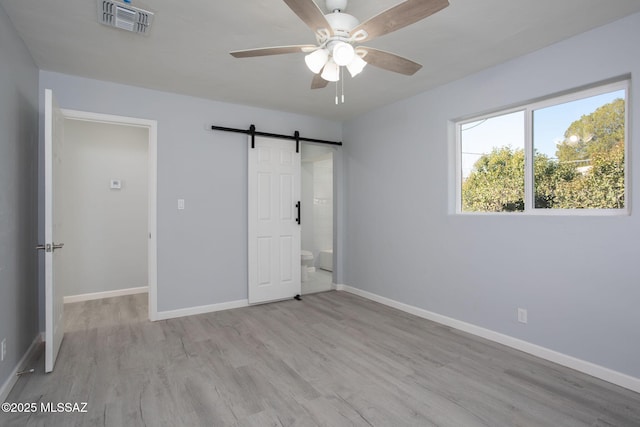 unfurnished bedroom featuring light wood-type flooring, a barn door, ceiling fan, and ensuite bathroom