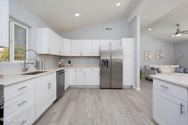 kitchen with stainless steel appliances, white cabinetry, lofted ceiling, and sink