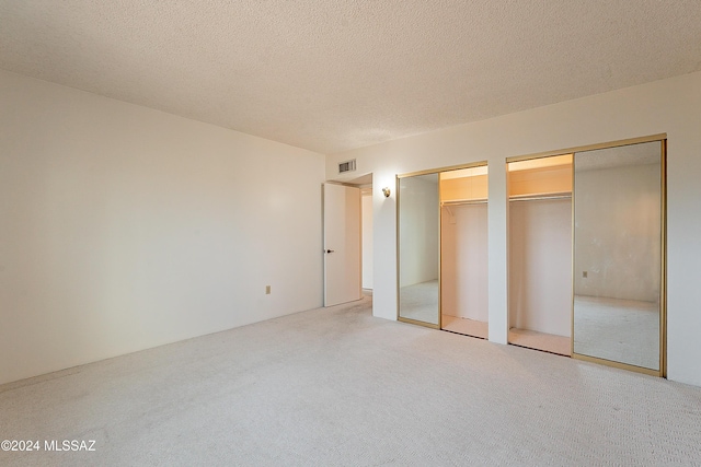 unfurnished bedroom with a textured ceiling and multiple closets