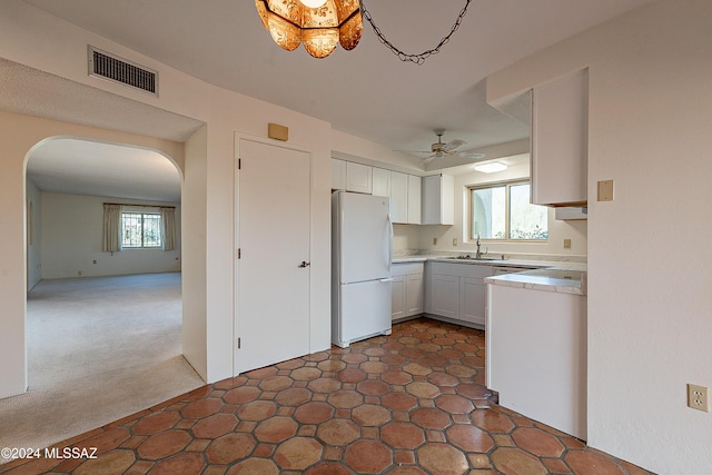 kitchen with sink, dark colored carpet, plenty of natural light, white fridge, and white cabinets