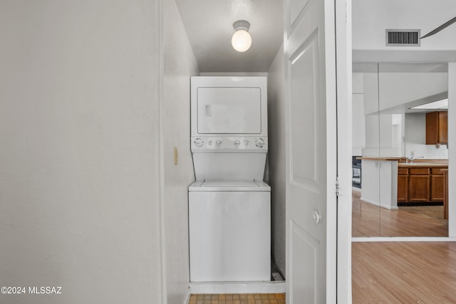 laundry room with light hardwood / wood-style floors, stacked washing maching and dryer, and sink