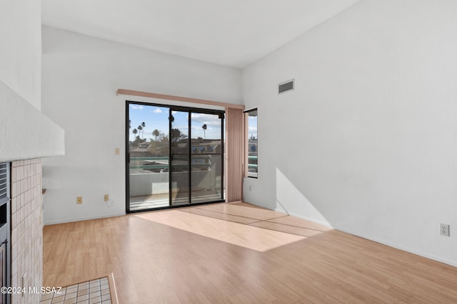 empty room with light wood-type flooring and a brick fireplace