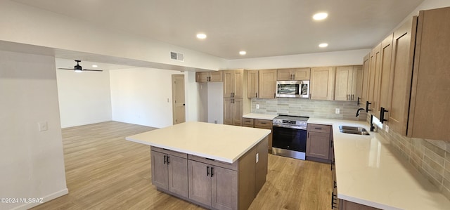 kitchen with stainless steel appliances, a kitchen island, ceiling fan, and light hardwood / wood-style flooring