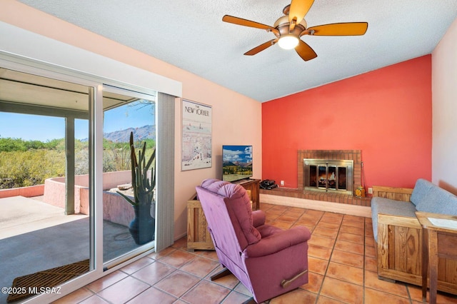 living room with ceiling fan, a mountain view, a textured ceiling, a fireplace, and light tile patterned flooring