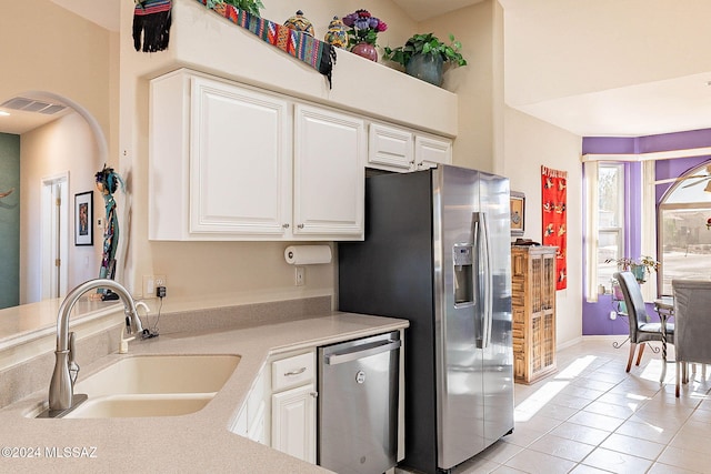 kitchen with arched walkways, stainless steel appliances, light countertops, white cabinetry, and a sink