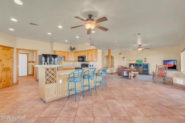 kitchen featuring light tile patterned floors, ceiling fan, a kitchen breakfast bar, black appliances, and light brown cabinetry