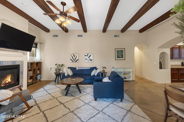 living room with beam ceiling, a tiled fireplace, and ceiling fan