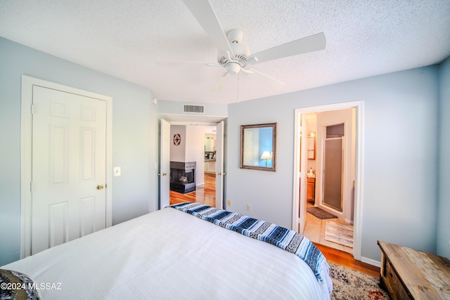 bedroom featuring a textured ceiling, ceiling fan, light hardwood / wood-style floors, and ensuite bathroom