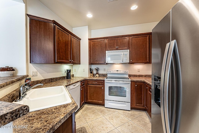 kitchen with sink, light tile patterned floors, dark stone counters, and appliances with stainless steel finishes