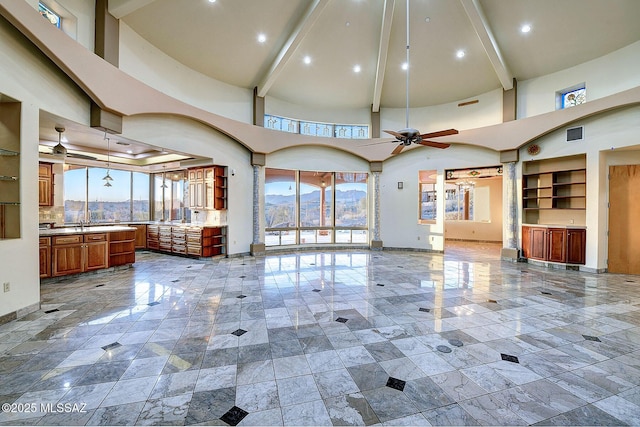 unfurnished living room featuring ceiling fan, beam ceiling, and a towering ceiling