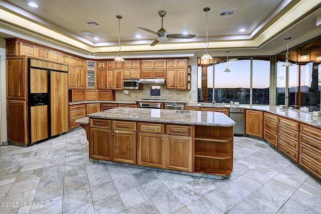 kitchen with ceiling fan, pendant lighting, a kitchen island, built in appliances, and a tray ceiling