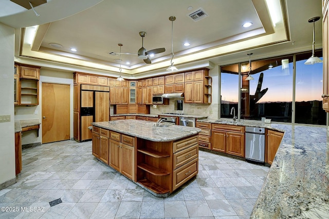 kitchen with pendant lighting, paneled built in fridge, a raised ceiling, and an island with sink