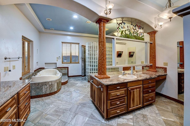 bathroom with tiled bath, a tray ceiling, vanity, and decorative columns