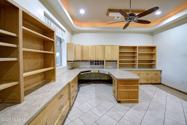 interior space featuring ceiling fan, a raised ceiling, light tile patterned flooring, a kitchen island, and built in desk