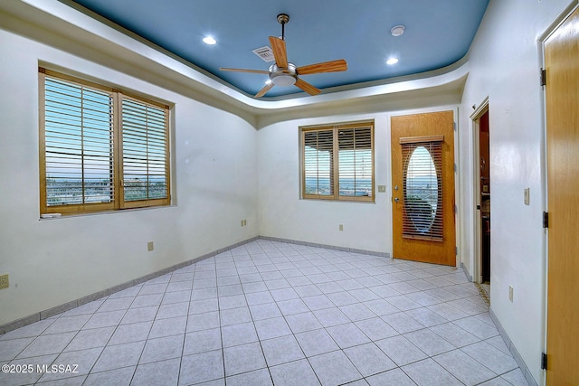 tiled empty room featuring a raised ceiling and ceiling fan