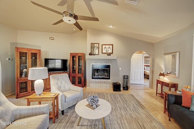 living room with light tile patterned floors, a fireplace, arched walkways, ceiling fan, and vaulted ceiling