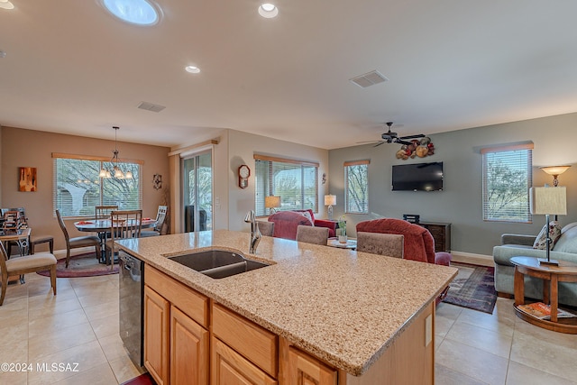 kitchen with dishwasher, sink, light stone counters, a center island with sink, and ceiling fan with notable chandelier