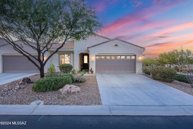 view of front facade with an attached garage, a tile roof, concrete driveway, and stucco siding