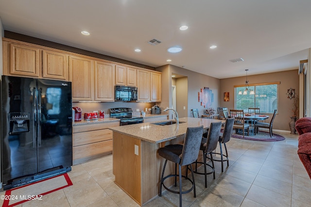 kitchen with light stone countertops, sink, black appliances, light tile patterned floors, and a center island with sink