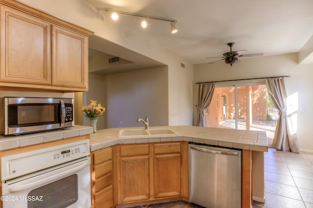 kitchen with light tile patterned floors, stainless steel appliances, a sink, a ceiling fan, and tile counters