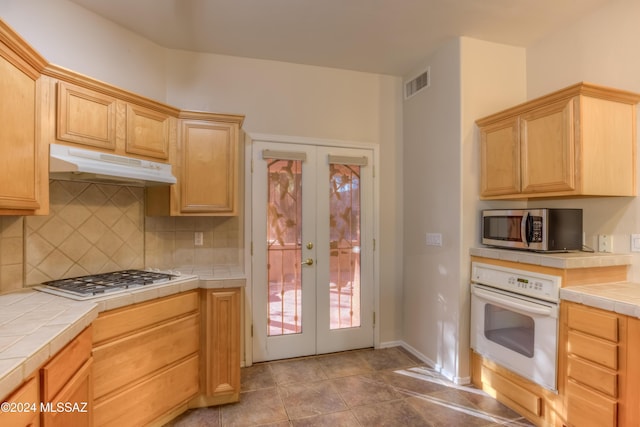 kitchen featuring under cabinet range hood, white appliances, visible vents, french doors, and tile counters