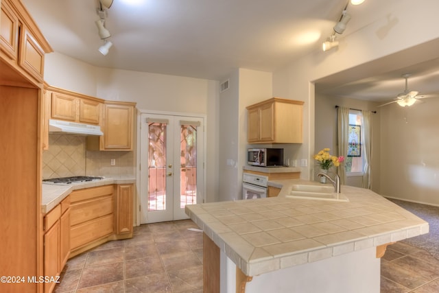 kitchen featuring under cabinet range hood, a sink, white oven, tile counters, and stainless steel microwave