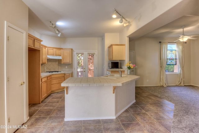 kitchen featuring under cabinet range hood, white gas stovetop, tile counters, tasteful backsplash, and stainless steel microwave