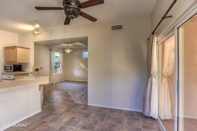 kitchen with visible vents, tile countertops, stainless steel microwave, light brown cabinetry, and a sink