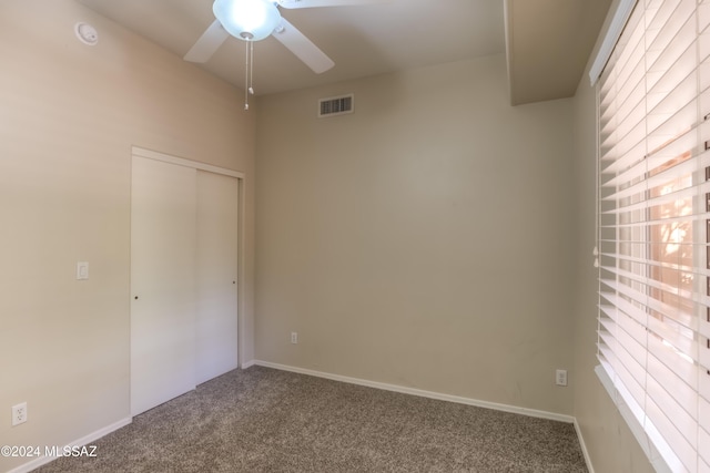 empty room with plenty of natural light, visible vents, dark carpet, and a ceiling fan