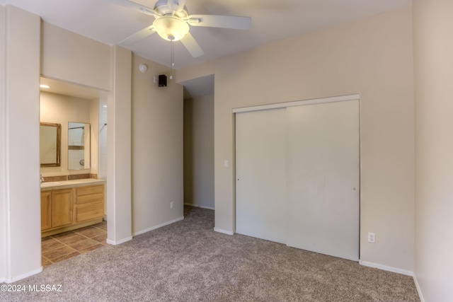 unfurnished bedroom with a closet, light colored carpet, a ceiling fan, a sink, and ensuite bath