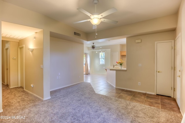 empty room featuring light tile patterned flooring, light colored carpet, a ceiling fan, baseboards, and visible vents