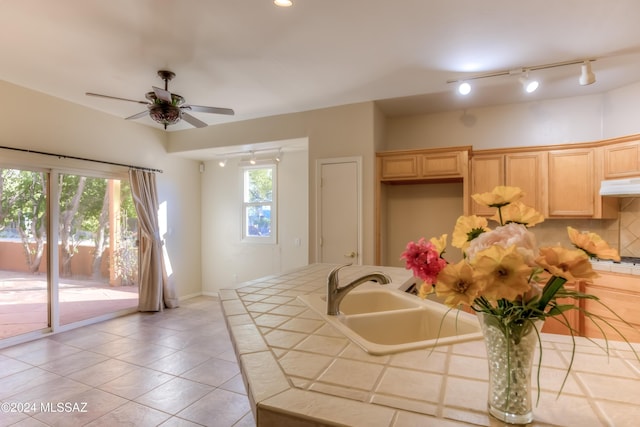 kitchen featuring tile countertops, backsplash, light brown cabinets, a sink, and under cabinet range hood