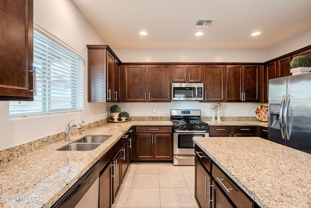 kitchen featuring sink, light tile patterned floors, appliances with stainless steel finishes, light stone counters, and dark brown cabinetry