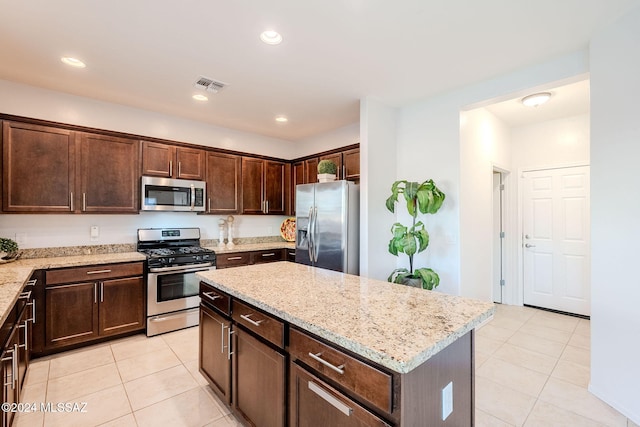 kitchen with a kitchen island, light stone counters, stainless steel appliances, and light tile patterned flooring