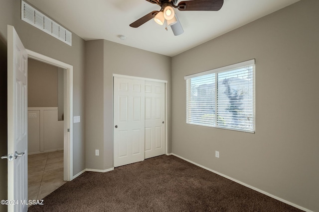 unfurnished bedroom with ceiling fan, a closet, and dark colored carpet