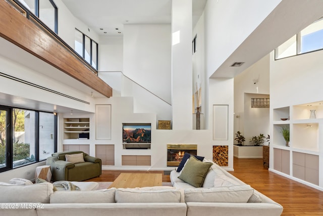 living room featuring hardwood / wood-style flooring, a towering ceiling, a wealth of natural light, and built in shelves