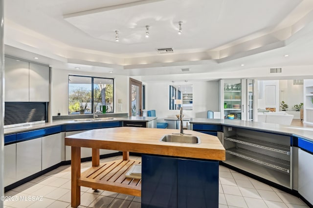 kitchen featuring butcher block counters, sink, a center island, light tile patterned floors, and a tray ceiling