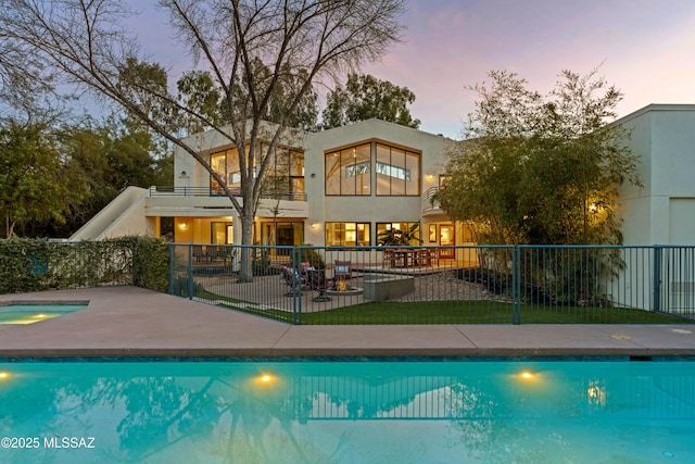 back house at dusk featuring a swimming pool with hot tub and a patio