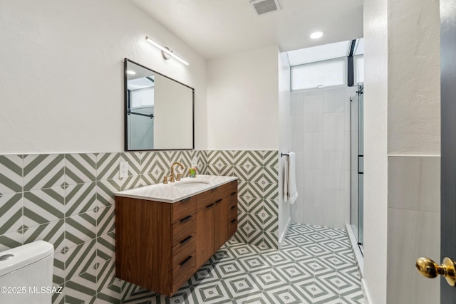 bathroom featuring tile walls, vanity, a shower with door, and toilet