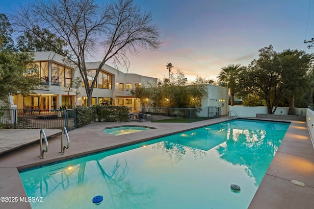 pool at dusk featuring an in ground hot tub and a patio