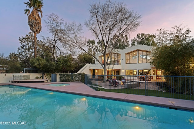 pool at dusk with a hot tub and a patio