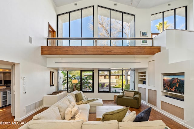 living room featuring a towering ceiling, wood-type flooring, beverage cooler, and built in shelves