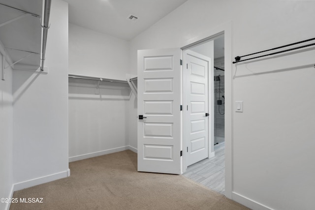 walk in closet with light carpet and vaulted ceiling