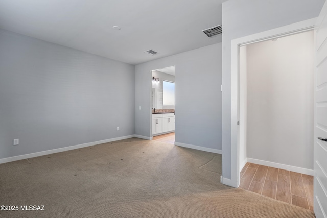 unfurnished bedroom featuring light carpet and ensuite bathroom