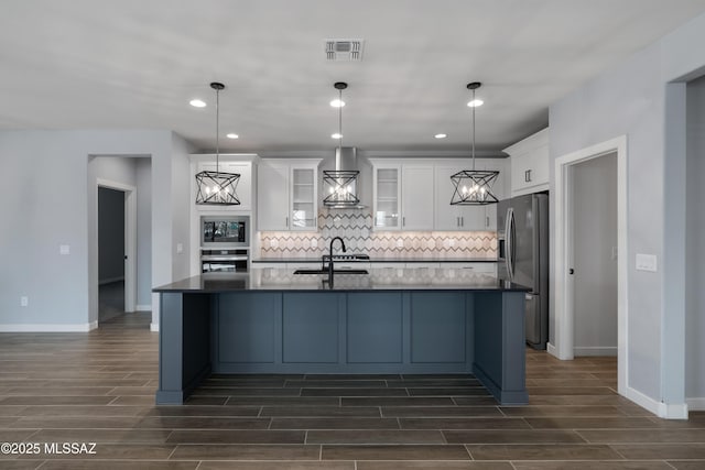 kitchen featuring wall chimney range hood, stainless steel appliances, decorative backsplash, white cabinets, and decorative light fixtures