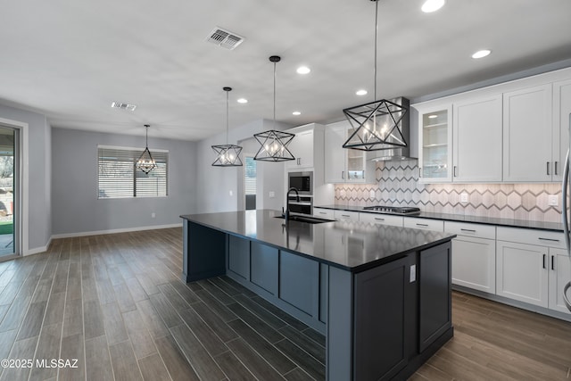 kitchen with pendant lighting, white cabinetry, sink, and a large island with sink