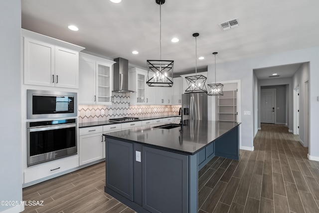 kitchen with appliances with stainless steel finishes, decorative light fixtures, sink, white cabinets, and wall chimney exhaust hood