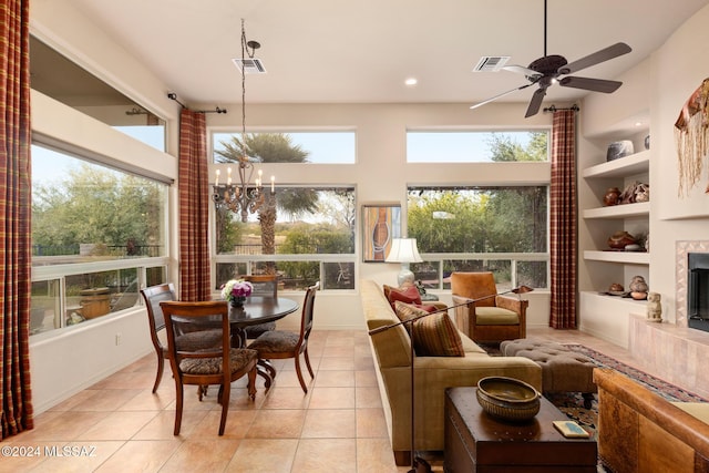 sunroom featuring a tile fireplace, ceiling fan with notable chandelier, and a healthy amount of sunlight